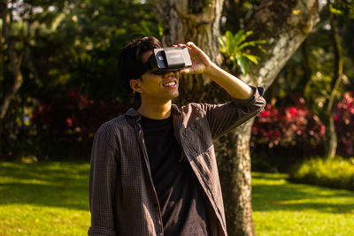 Young man looking through virtual reality while standing at park