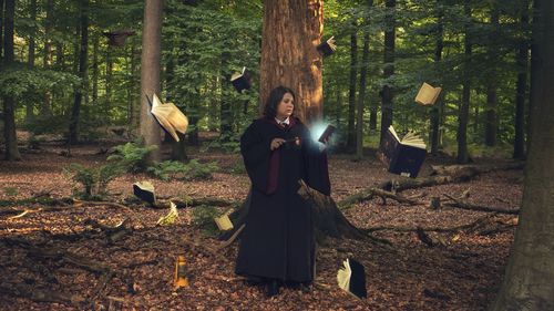 Portrait of young woman standing by tree trunk in forest