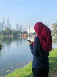 Woman in hijab using mobile phone at lakeshore in city