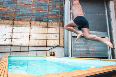 Low section of shirtless man jumping over swimming pool