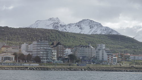 Scenic view of river by buildings and mountains against sky