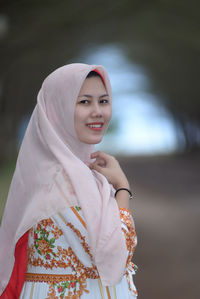 Portrait of young woman standing against trees