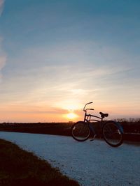 Bicycle parked on road against sky during sunset