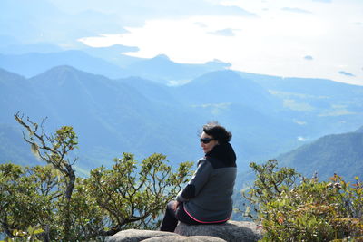 Side view of woman sitting on mountain against sky