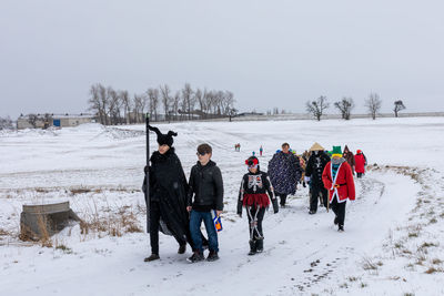 People on snow covered field against sky