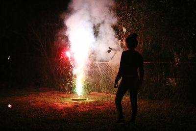 Silhouette woman standing by firework on field at night