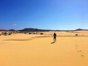 Man walking in desert against clear blue sky