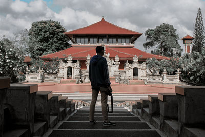 Rear view of man standing by building against sky