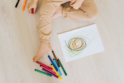 Close-up of a boy's hand sitting at home on the floor and drawing a drawing with colored pencils