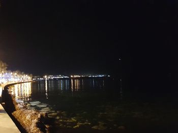 Illuminated city by river against clear sky at night