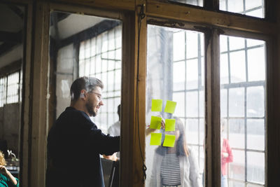 Businessman writing on adhesive note while having meeting with female programmer at creative office