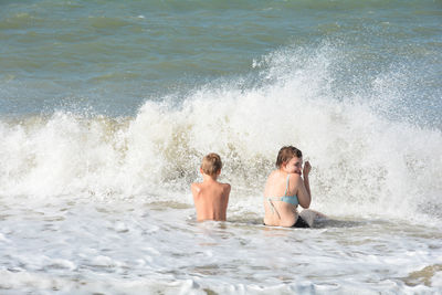 Two children sit on the sandy beach in the middle of the waves by the sea, netherlands