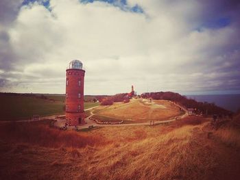 Lighthouse on grassy field against cloudy sky