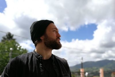 Confident bearded man looking away while standing against cloudy sky