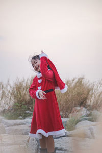 Girl wearing red dress while standing on rocks against sky during christmas