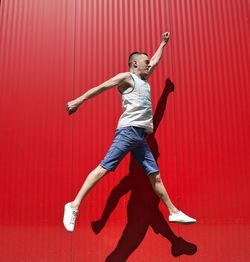 Full length of man jumping against red wall