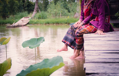 Low section of women sitting on pier over lake