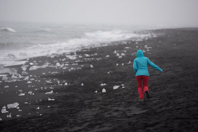 Rear view of woman running at beach during winter