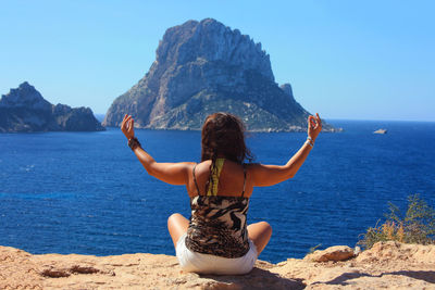 Rear view of woman on rock by sea against sky