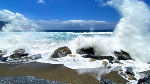 Waves splashing on rocks against sky