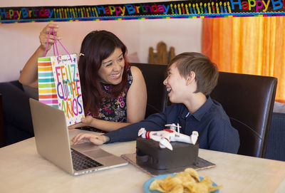 Cheerful mother holding gift for son at home during birthday celebration