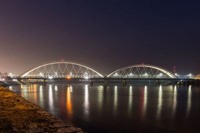 Illuminated bridge over river against sky at night