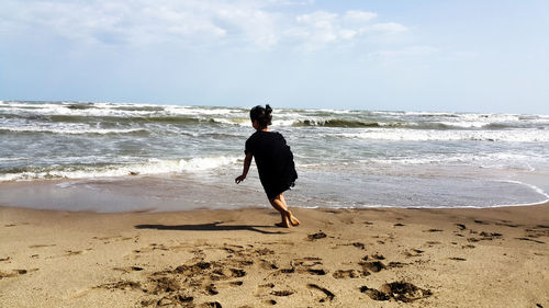 Rear view of woman on beach against sky