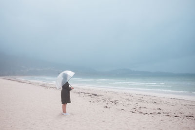 Rear view of woman standing on beach against sky