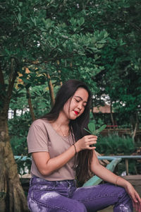 Beautiful young woman sitting against trees