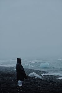 Rear view of man standing on beach against sky