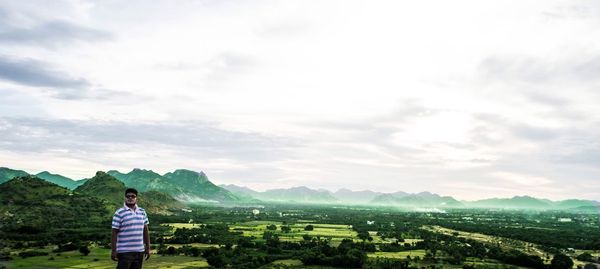 Man standing by green landscape against sky