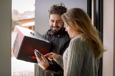 Female customer signing on smart phone while receiving package from delivery man