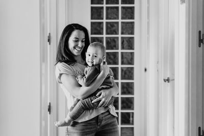 Smiling mother holding daughter at entrance of home