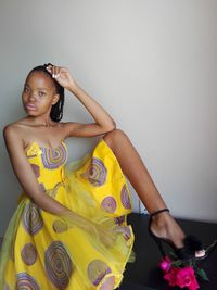 Portrait of young woman sitting against yellow wall