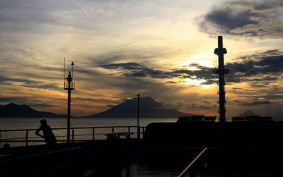 Silhouette street by sea against sky during sunset