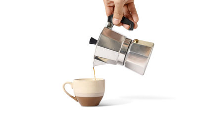 Low angle view of hand pouring coffee cup against white background