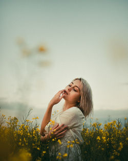 Young woman with yellow flowers on field against sky