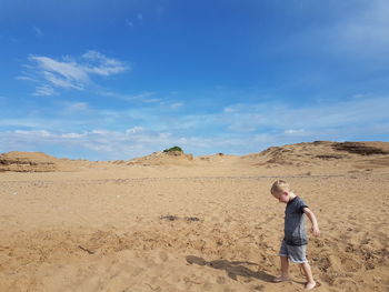 Side view of boy walking on sandy beach against blue sky