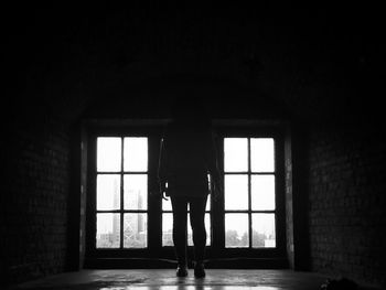 Rear view of woman standing against window in empty room