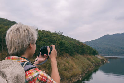 Man photographing lake and mountains against sky