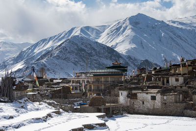 Snow covered houses by mountains against sky