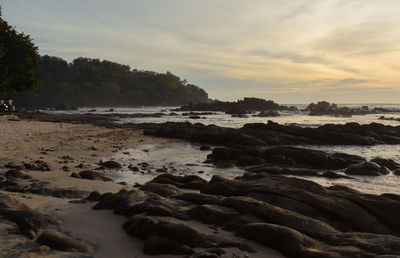 Rocks on beach against sky during sunset