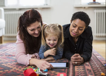 Smiling lesbian couple and girl using digital tablet at home