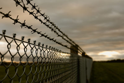 Low angle view of barbed wire fence on field against sky