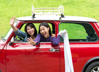 Portrait of smiling happy friends waving while sitting in car