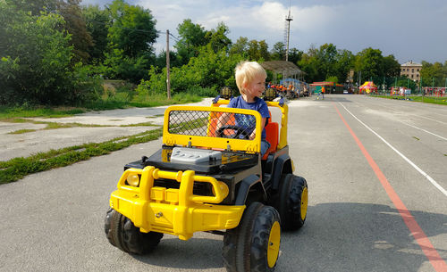 Boy sitting in toy car on road in city