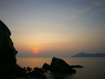 Scenic view of sea and cliff against sky during sunset