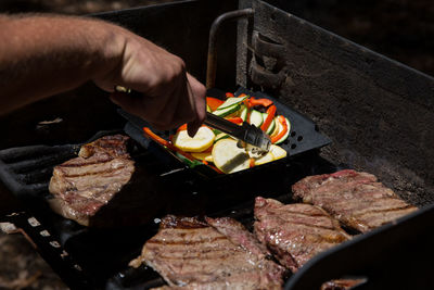 Cropped image of man preparing meat on barbeque grill at park