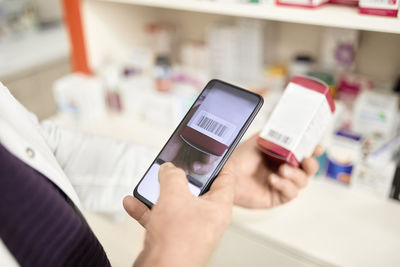 Pharmacist scanning barcode of medicine box through smart phone at pharmacy store