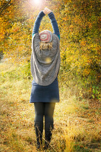 Rear view of woman with arms raised standing against autumn trees